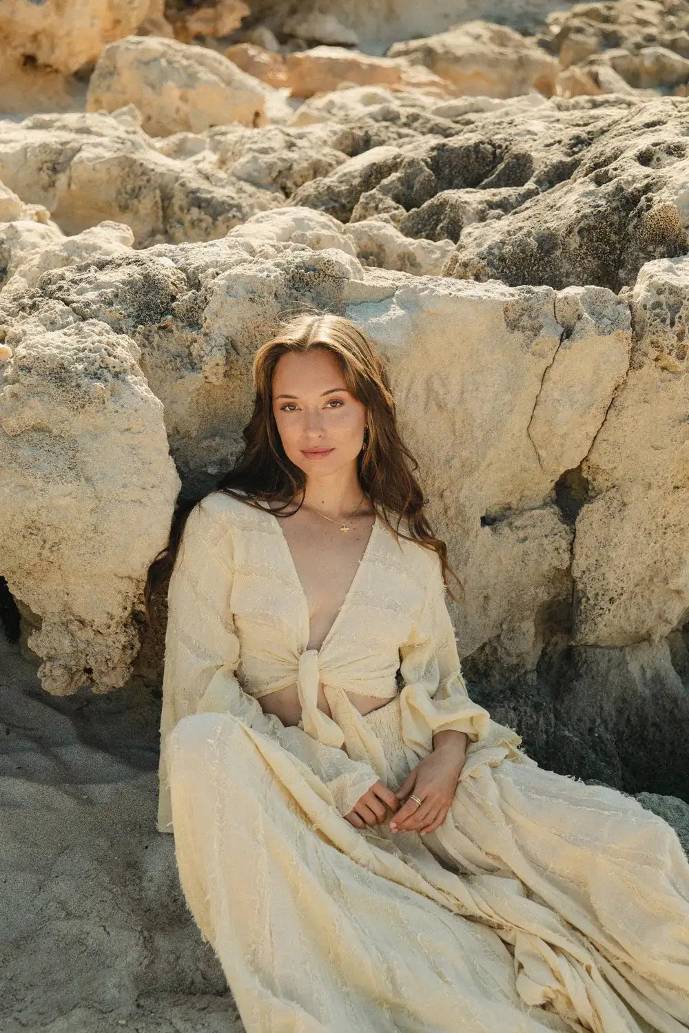 Mujer sentada en piedras con top boho esencia mangas acampanadas amarillas, mostrando un estilo bohemio y elegante.