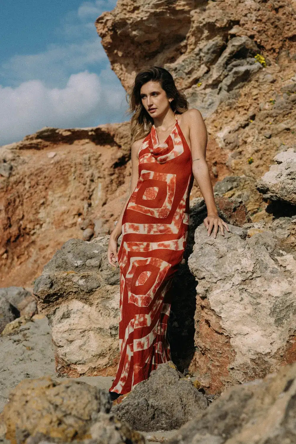 Modelo luciendo un vestido de gasa geométrica en un paisaje rocoso al aire libre.